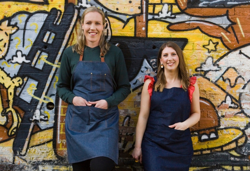 gem&ally-wearing-aprons-leaning-against-workshop-wall-01 Gem and Ally wearing their aprons, leaning against the workshop wall